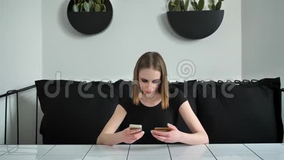 年轻漂亮的女人在电话里用卡片重写坐在沙发上黑白咖啡馆背景视频的预览图