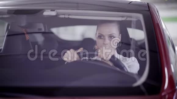 穿着白衬衫的美女坐在红色的车里在车库里四处张望视频的预览图