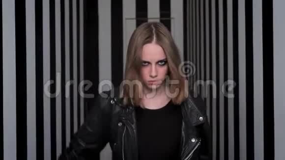 年轻漂亮的女人浓妆艳抹地走向相机脱下黑色夹克条纹走廊背景视频的预览图