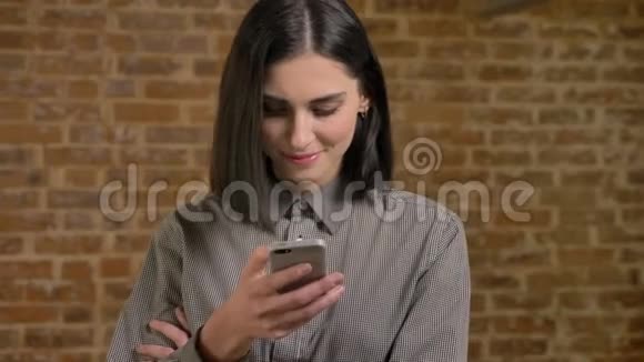 年轻美丽的女人的肖像棕色短发发短信微笑快乐砖墙背景视频的预览图