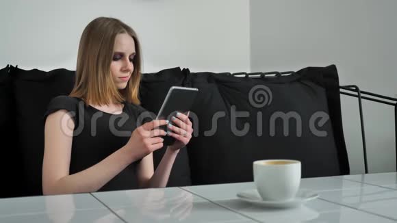 年轻漂亮的女人用平板电脑化妆坐在沙发上微笑着黑白咖啡背景视频的预览图