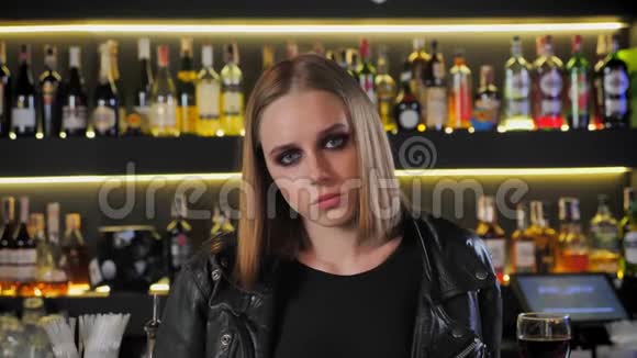 年轻漂亮的女人穿着黑色夹克浓妆艳抹在镜头里直视严肃坚定酒吧背景视频的预览图