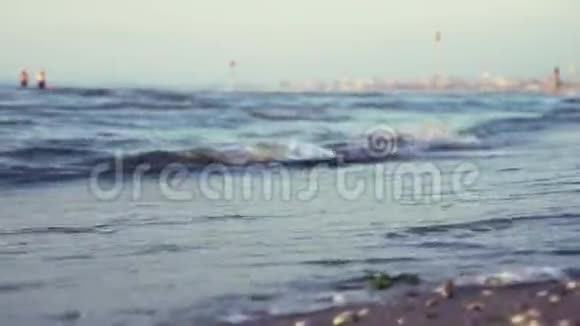 大海的小浪在岸边在晴朗的日子里有一座城市在背景下视频的预览图