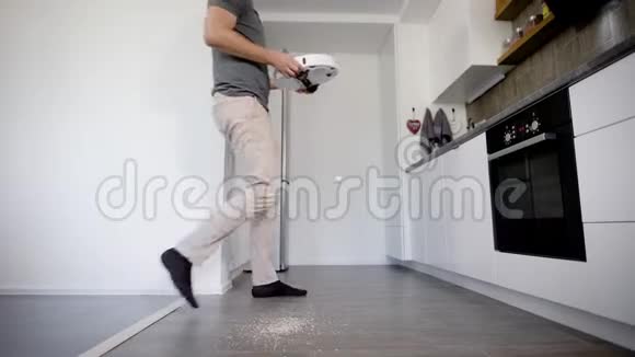 成年男子正在厨房的地板上放置圆形的机器人吸尘器打开它然后出去视频的预览图