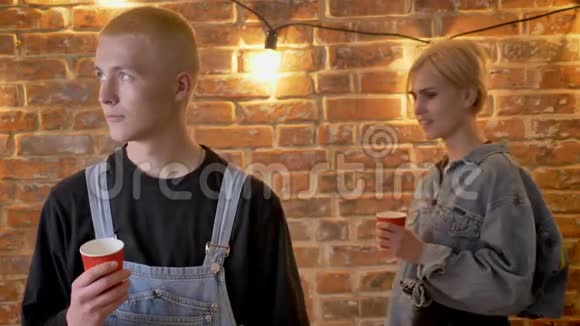 年轻有趣的男孩子正拿着杯子站着他的女朋友摸着他的肩膀呼号亲吻笑视频的预览图