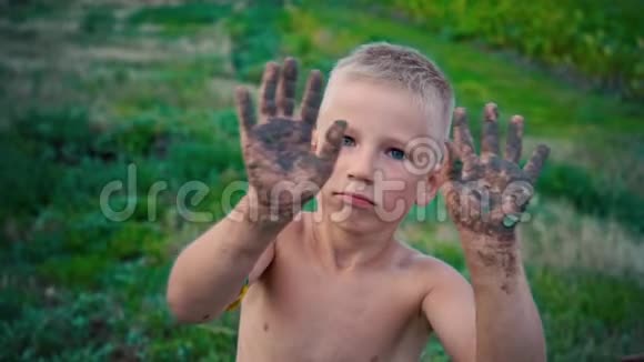 一个快乐的孩子从地球上露出脏手向不同的方向挥动脏手一个男孩涂在地上视频的预览图