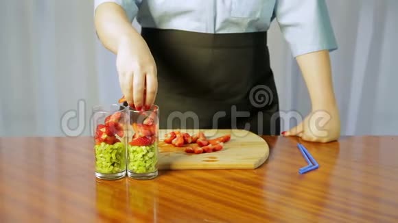 一个女人把碎奇异果片和成熟草莓放进玻璃杯里视频的预览图