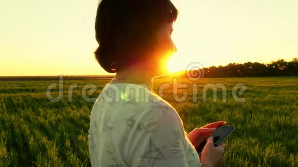 年轻有魅力的女人用智能手机在绿色草坪上的日落背景下慢动作视频的预览图