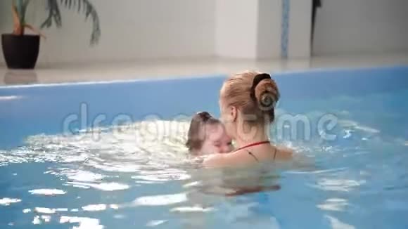 年轻的妈妈在游泳池里慢动作地和她的小女儿玩耍积极生活方式的体育家庭视频的预览图