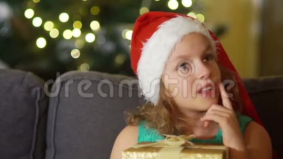 那个女孩许下圣诞节的愿望戴着圣诞帽的棕色眼睛女孩的亲密肖像手里拿着礼品盒圣诞节视频的预览图