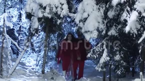 穿着红色衣服的可爱的男人和女人在白雪皑皑的冬林中慢慢移动视频的预览图
