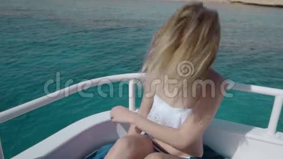 美丽的白种人女孩穿着比基尼戴着太阳镜坐在蓝色水晶海水的海洋游艇上视频的预览图