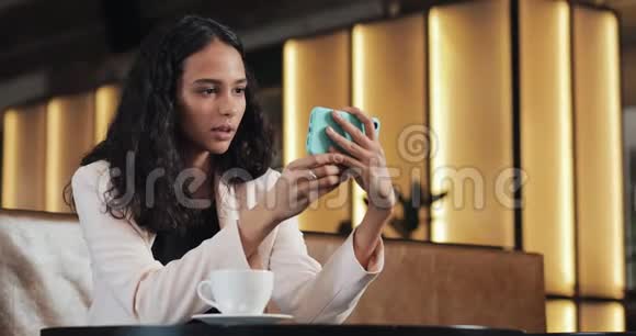 商务女性坐在舒适的咖啡馆里喝咖啡看智能手机上的视频视频的预览图