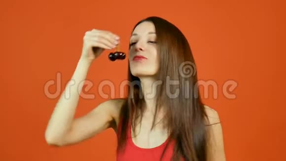 美丽的年轻性感女人吃深红色浆果在橙色背景在工作室健康营养视频的预览图