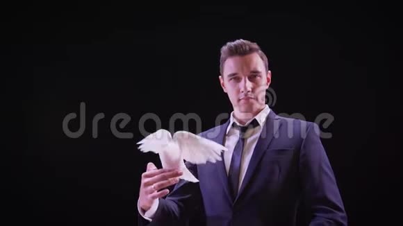 带着白鸽的年轻魔术师年轻英俊的黑发魔术师和他训练好的白鸽表演舞台服装视频的预览图