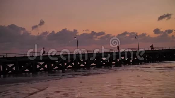 不可辨认的人在海岸的长墩上行走的剪影视频的预览图