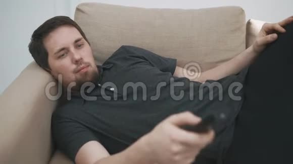 一个人躺在电视机前手里拿着遥控器他正在休息日看电影视频的预览图