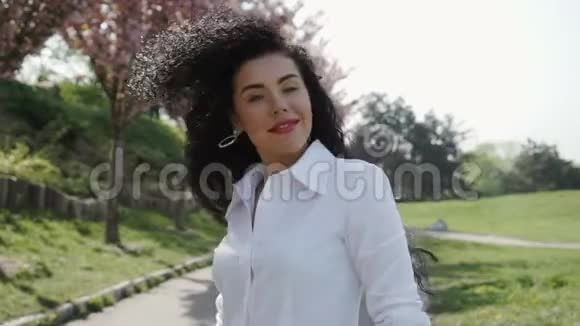 快乐的黑发女人卷着卷发看着镜头视频的预览图