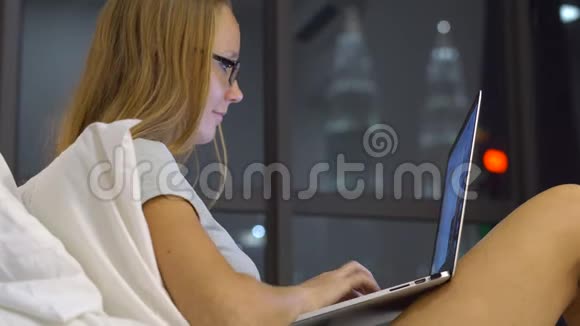 有趣的年轻女人戴着眼镜用笔记本电脑工作坐在床上笑着她在打字视频的预览图