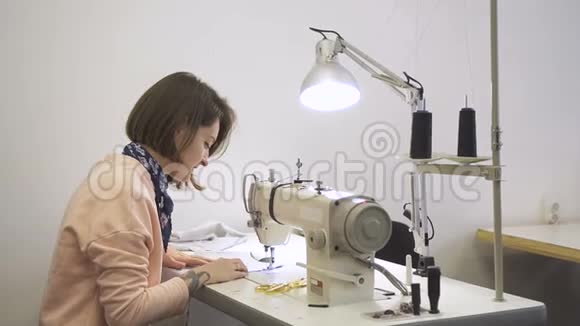 年轻的职业裁缝在工作过程中缝制衣服用缝纫机和布料用视频的预览图