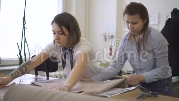 两名年轻妇女在缝纫车间的桌子上铺布女专业人员正在面料加工靠近视频的预览图