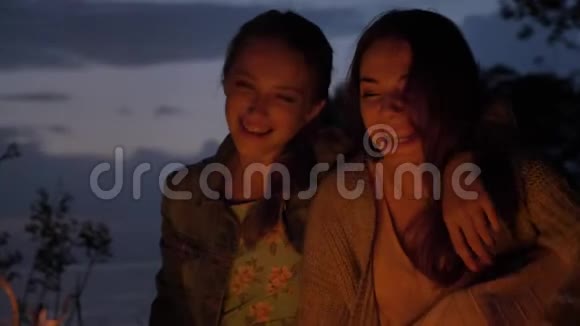 两个白种人年轻的女孩在晚上坐在大自然的炉火旁笑着微笑着视频的预览图
