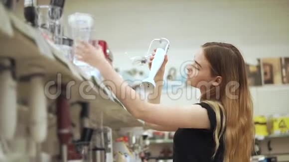 年轻的顾客女士正从商店的架子上拿着一个搅拌器和碗视频的预览图