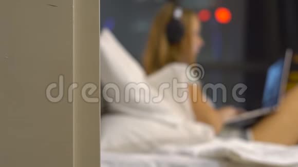 一位戴无线耳机的女士用笔记本电脑工作的剪影她坐在床上视频的预览图