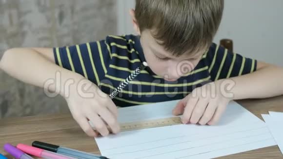 7岁的男孩穿着条纹t恤用铅笔和尺子在纸上画均匀的线条特写镜头视频的预览图