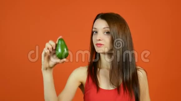红顶漂亮女孩的肖像长发手持暗绿色鳄梨在镜头前展示视频的预览图