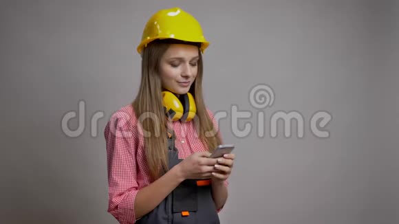 年轻可爱的女孩建设者正在她的智能手机短信沟通概念灰色背景视频的预览图
