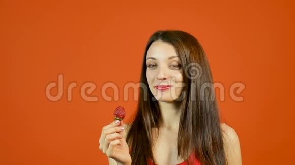 性感诱惑的成年女孩在工作室的橙色背景下吃红色成熟草莓视频的预览图