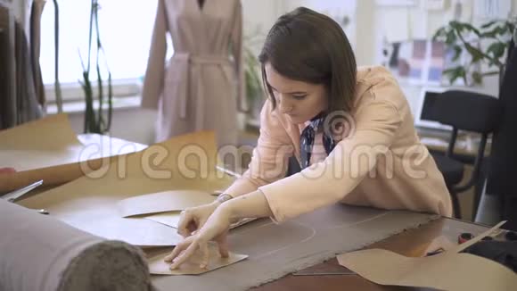 年轻的女裁缝正在用粉笔在纸巾上做记号站在缝纫室的桌子旁时装设计师在视频的预览图