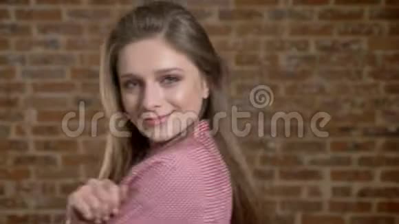 年轻漂亮的女孩正和她的肩膀跳舞玩头发调情看镜头砖背景视频的预览图