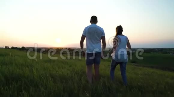 浪漫的年轻幸福的新婚夫妇在夕阳下的草地上散步视频的预览图