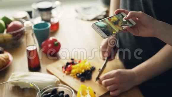 为沙拉切菜的男人的特写镜头和他的女朋友在智能手机摄像头上为社交拍照视频的预览图