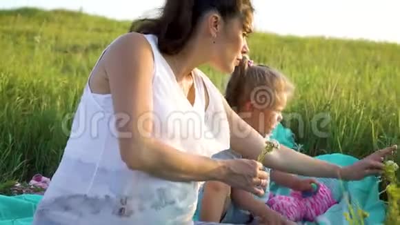 美丽快乐的母亲和女儿分享爱一起在草地上的毯子上看花视频的预览图