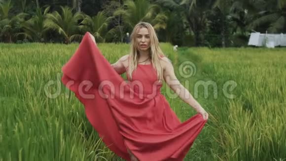 一个年轻女孩沿着稻田走着挥舞着她那飘逸的丝绸裙子风吹起她的头发视频的预览图