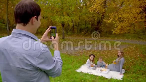 秋天在公园里野餐爸爸给他的妻子和孩子拍照视频的预览图