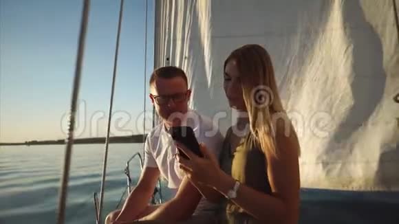 年轻男女正在考虑智能手机上的照片坐在帆船上视频的预览图