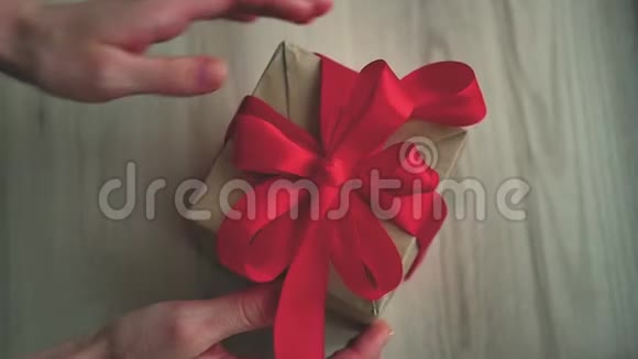 棕色礼品盒和带标签的红色丝带在木桌上女人的手解开丝带视频的预览图
