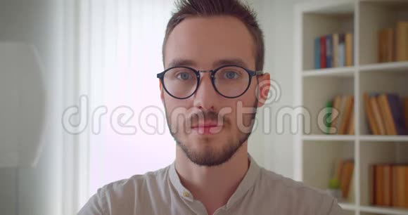 年轻英俊的白种人男学生戴着眼镜在室内的公寓里看着照相机的特写照片视频的预览图