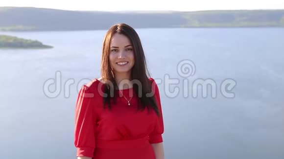 美丽的欧洲女人穿着红色的裙子对着大河岸边的镜头微笑视频的预览图