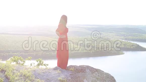 美丽的欧洲女人在大河岸边玩她的红色裙子令人惊叹的背景巨大的河流日落视频的预览图