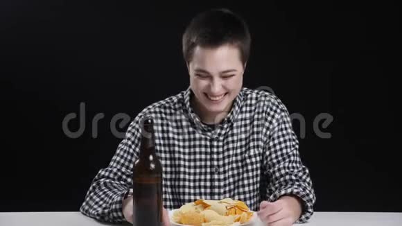 年轻的男性女孩吃完薯片喝完啤酒微笑笑饮食观念黑背景视频的预览图