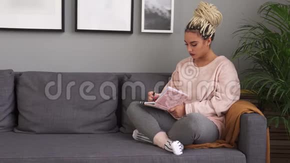 漂亮的女孩坐在舒适的沙发上写着笔记本视频的预览图