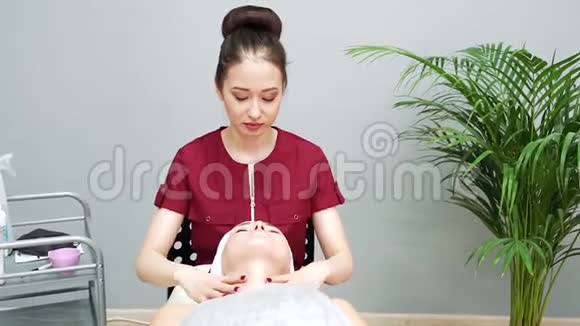 医疗诊所年轻女性得到专业的面部护理美容师在面膜后做面部按摩视频的预览图