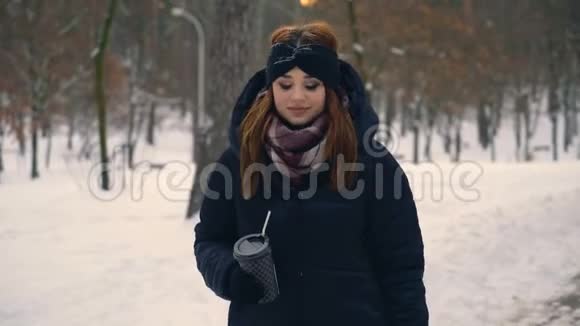 红姜发女走在雪地公园女孩从纸杯里喝咖啡冬晚4K视频的预览图