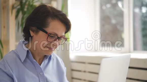 戴眼镜的成熟女人在笔记本电脑的舒适办公室工作视频的预览图