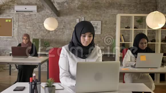 三个年轻的穆斯林妇女戴着头巾坐在现代办公室的笔记本电脑上打字生病的妇女咳嗽和工作视频的预览图